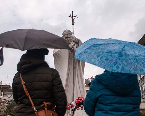 Zwei Frauen mit Regenschirmen schauen auf ein Denkmal